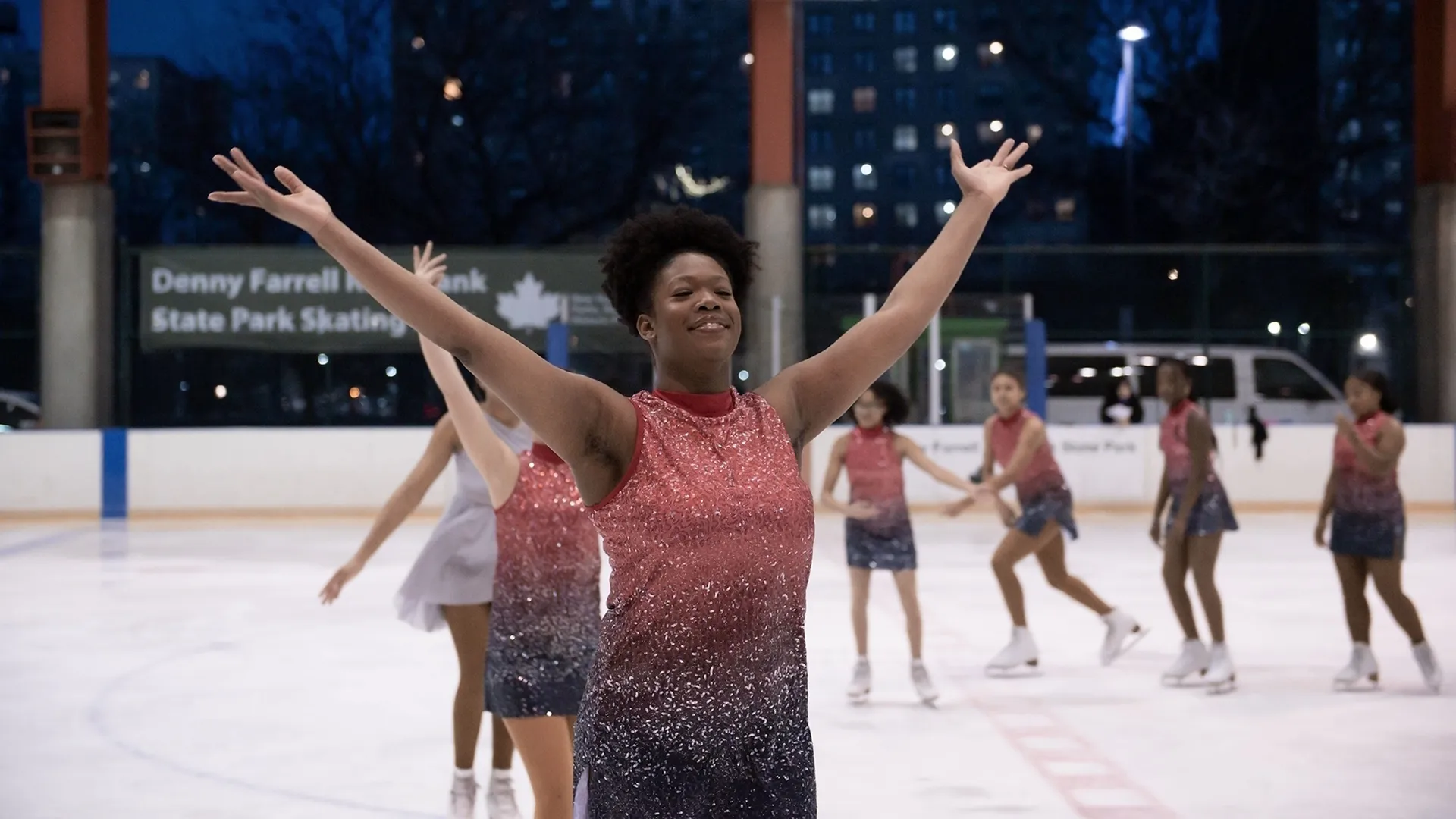 A group of Black girls in figure skating outfits skate on a rink