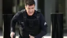 Officer Nolan, played by Nathan Fillion, moves in tactical gear with gun drawn in a tense scene from The Rookie.