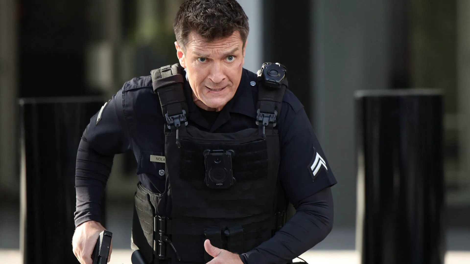Officer Nolan, played by Nathan Fillion, moves in tactical gear with gun drawn in a tense scene from The Rookie.