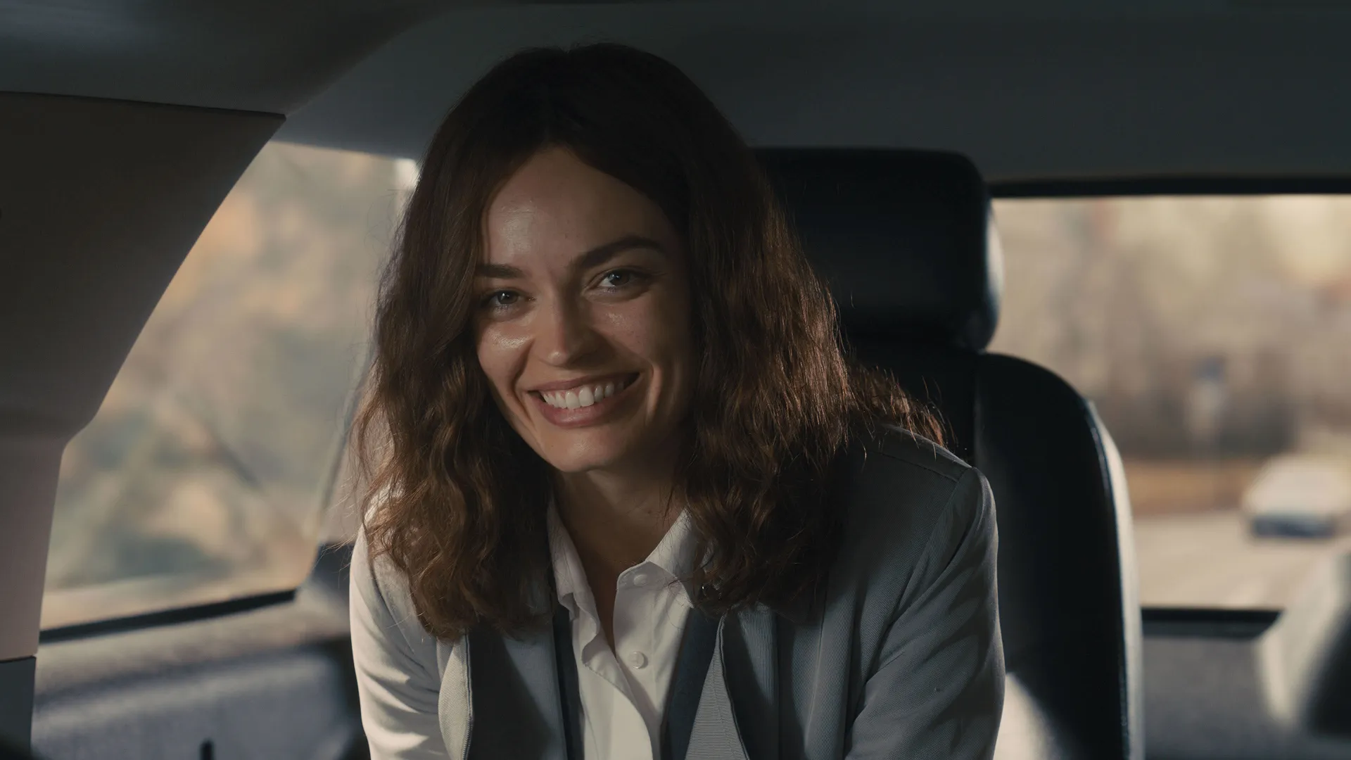 Ella (Emma Mackey) smiling in the back seat of a car.