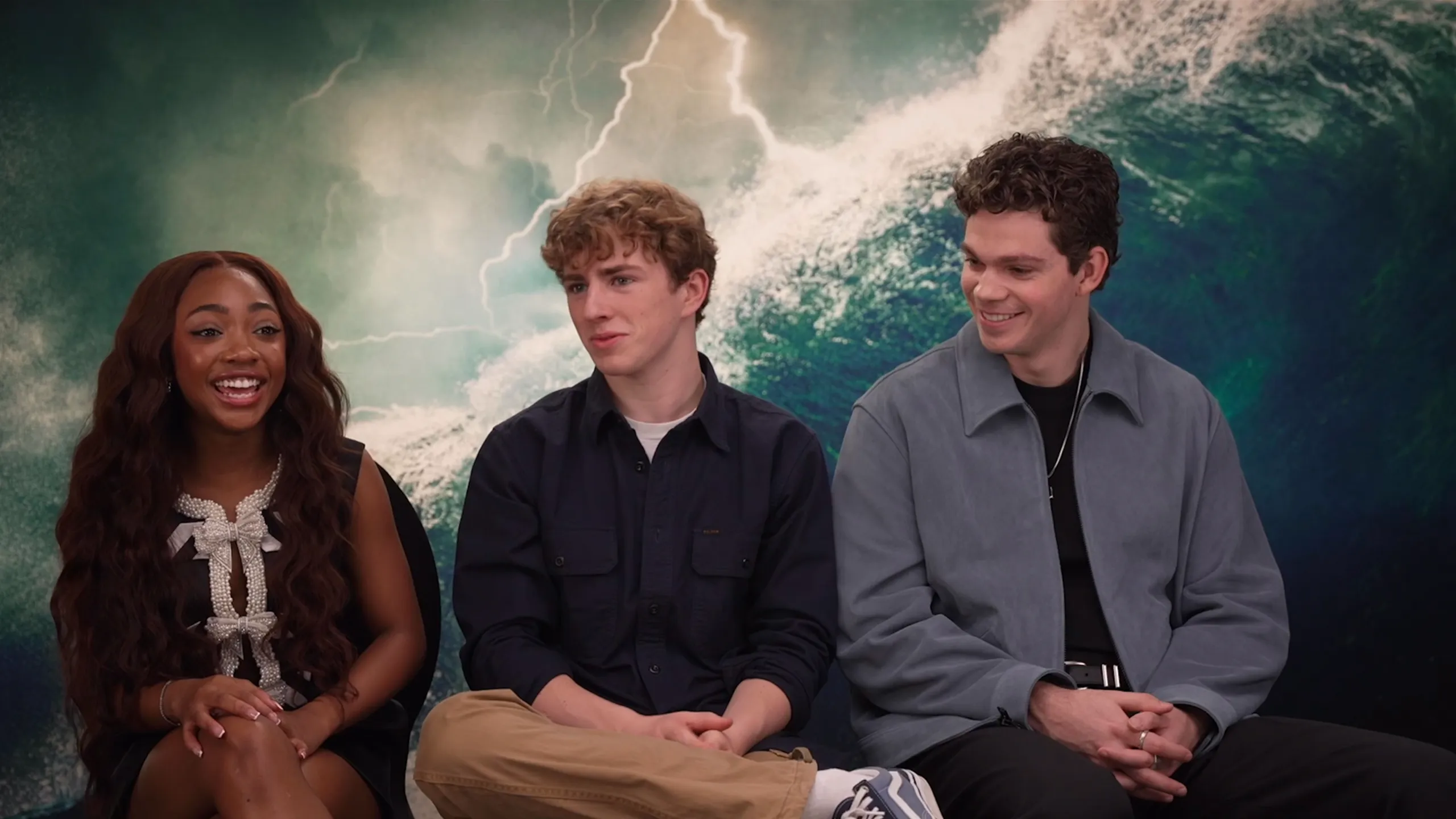 Percy Jackson and The Olympians cast members Leah Jeffries, Walker Scobell, and Daniel Diemer sat for an interview, with an ocean waves background