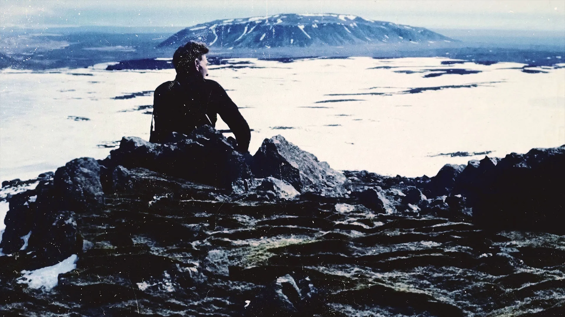 Key art for Time and Water featuring a lone figure sitting on rocks overlooking a snowy landscape and distant mountain.
