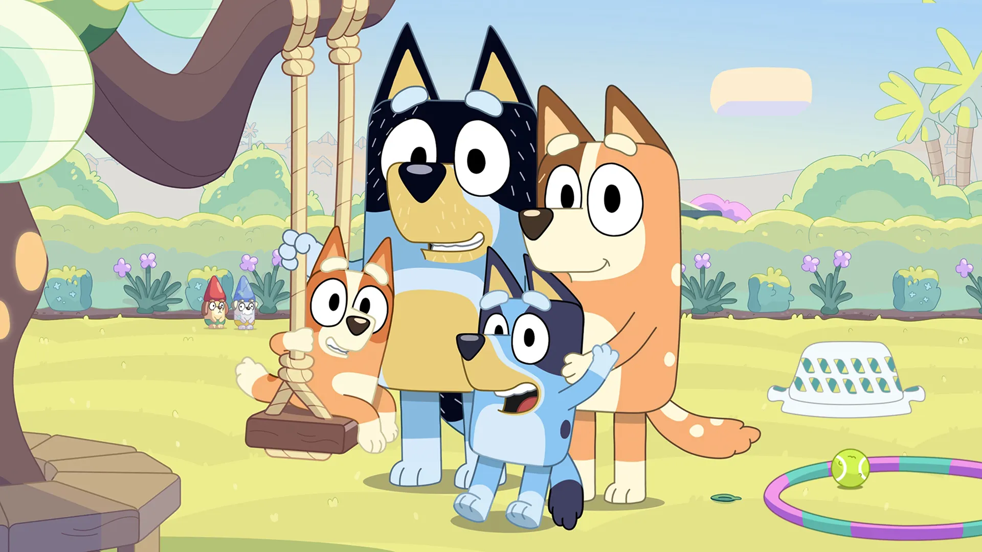 The Heeler family from Bluey—Bandit, Chilli, Bluey, and Bingo—smile together in their sunny backyard near a tree swing and garden toys.