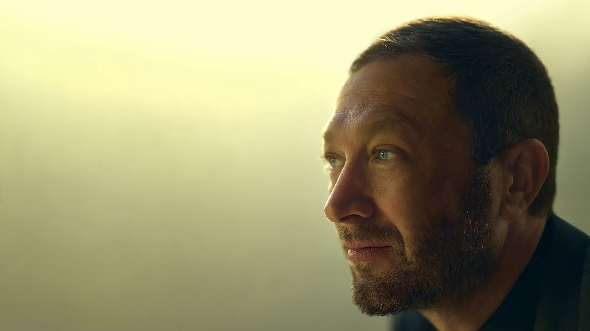 Close de perfil de um pensativo Richard "Richie" Jerimovich (Ebon Moss-Bachrach) olhando para o horizonte contra um fundo amarelo suave e brilhante.