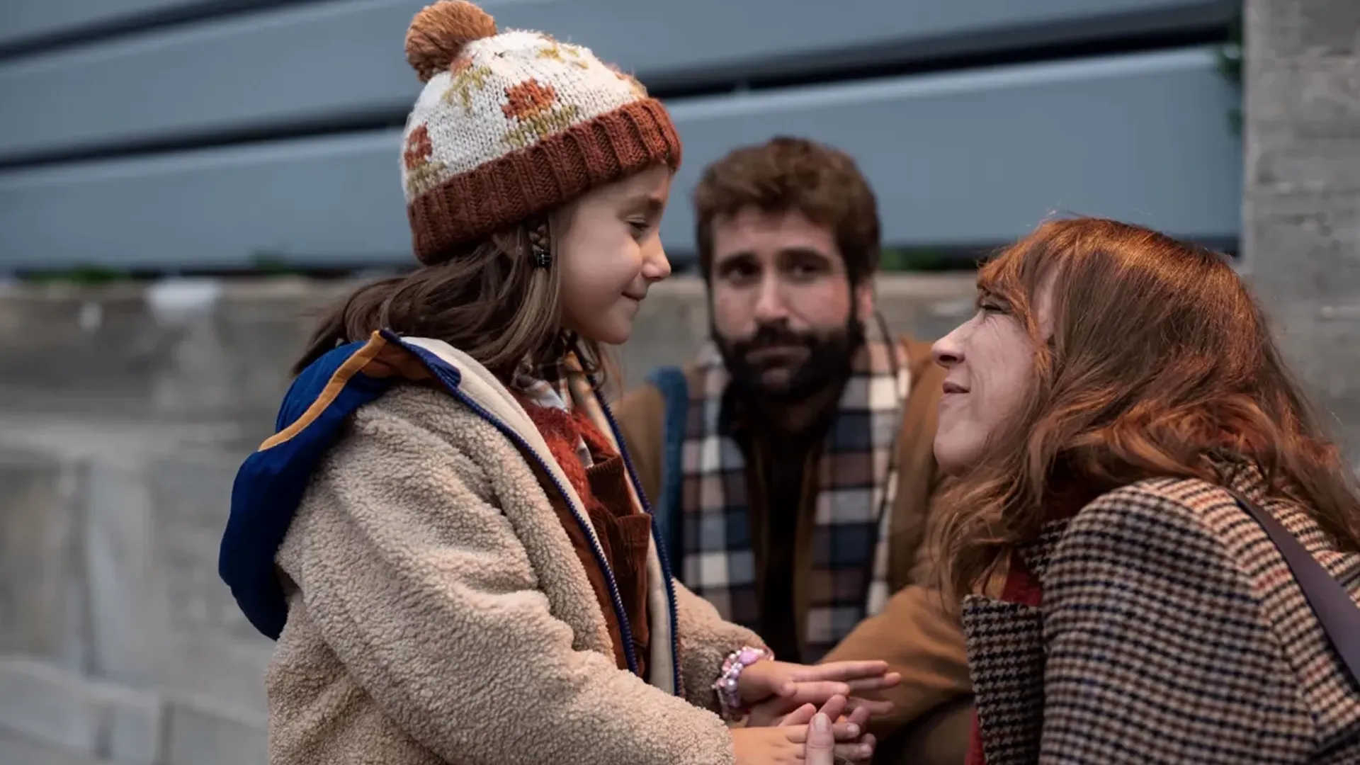 Cris (Lorena López) crouches down and smiles at her daughter Cloe, with Cloe's father Diego (Ricard Farré) watching them.