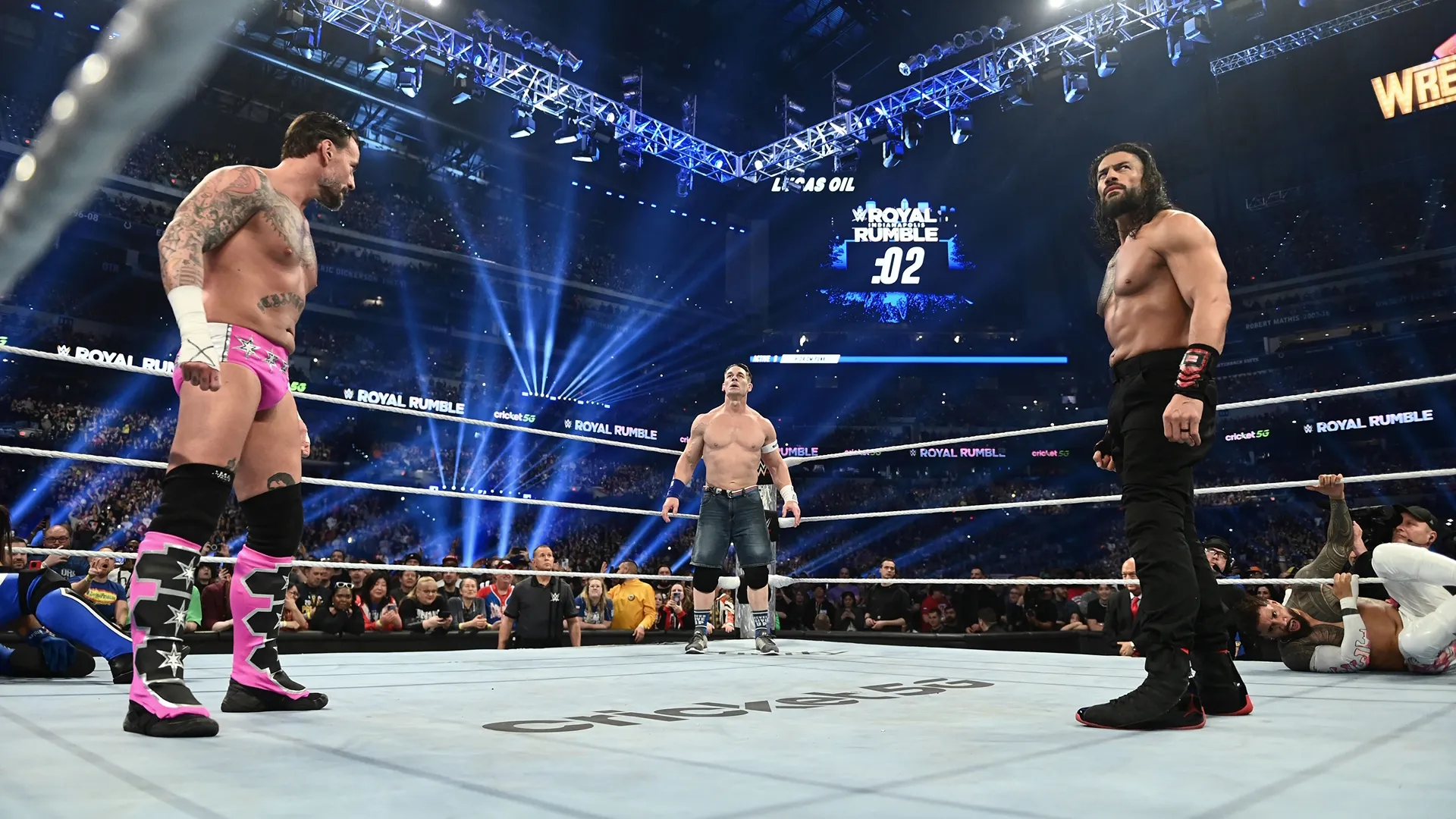 Wrestlers CM Punk, John Cena, and Roman Reigns standing in the ring at WWE Royal Rumble