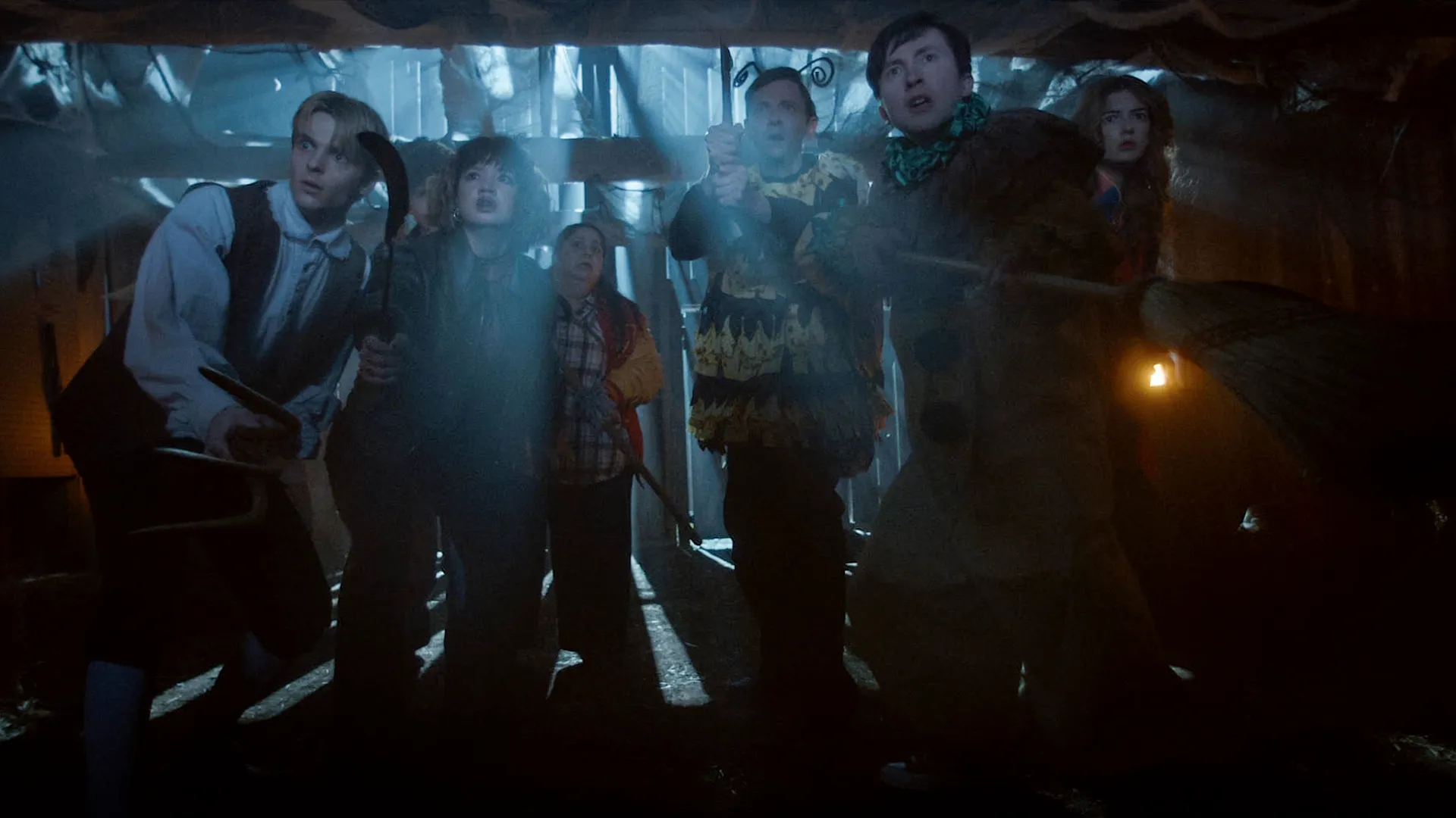 A group of friends, including Will (Ethan Herisse), Lisa (Chloe Caro), and Sarah (Madison Ekstrand), look up in fear and confusion within a dimly lit barn in Carved.