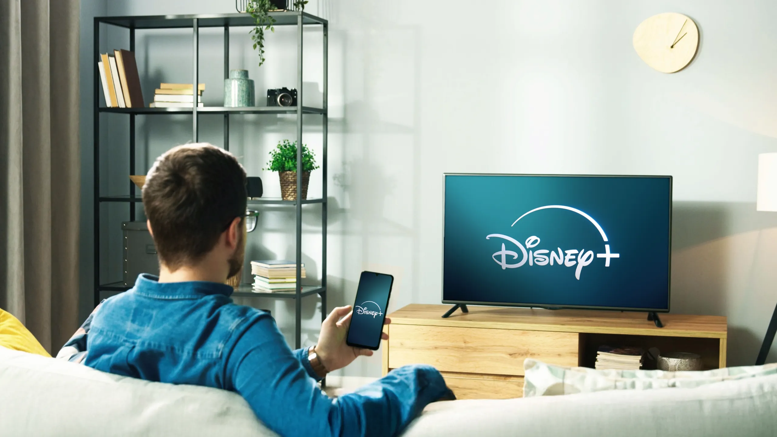 Man watching television in his living room, the television showcases the Disney+ start screen