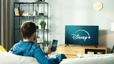 Man watching television in his living room, the television showcases the Disney+ start screen