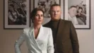 Wayne Rooney and Coleen Rooney pose together in front of a wall with three family portraits hanging on it
