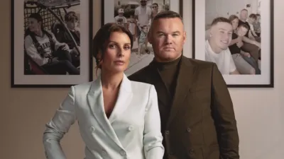 Wayne Rooney and Coleen Rooney pose together in front of a wall with three family portraits hanging on it