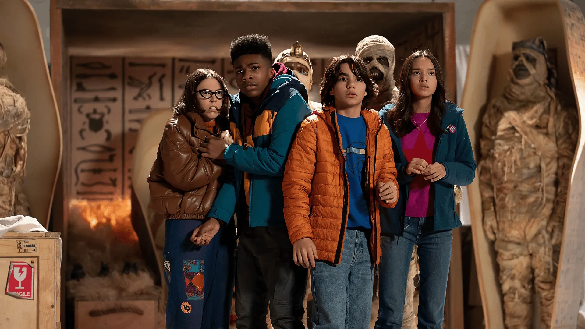 Buzzy (Melanie Brook), Gilbert (Christian J. Simon), Marshall (Malachi Barton), and Amy (Sophia Hammons) stand frozen with wide-eyed, terrified expressions inside a tomb, flanked by ancient Egyptian sarcophagi and reanimated mummies
