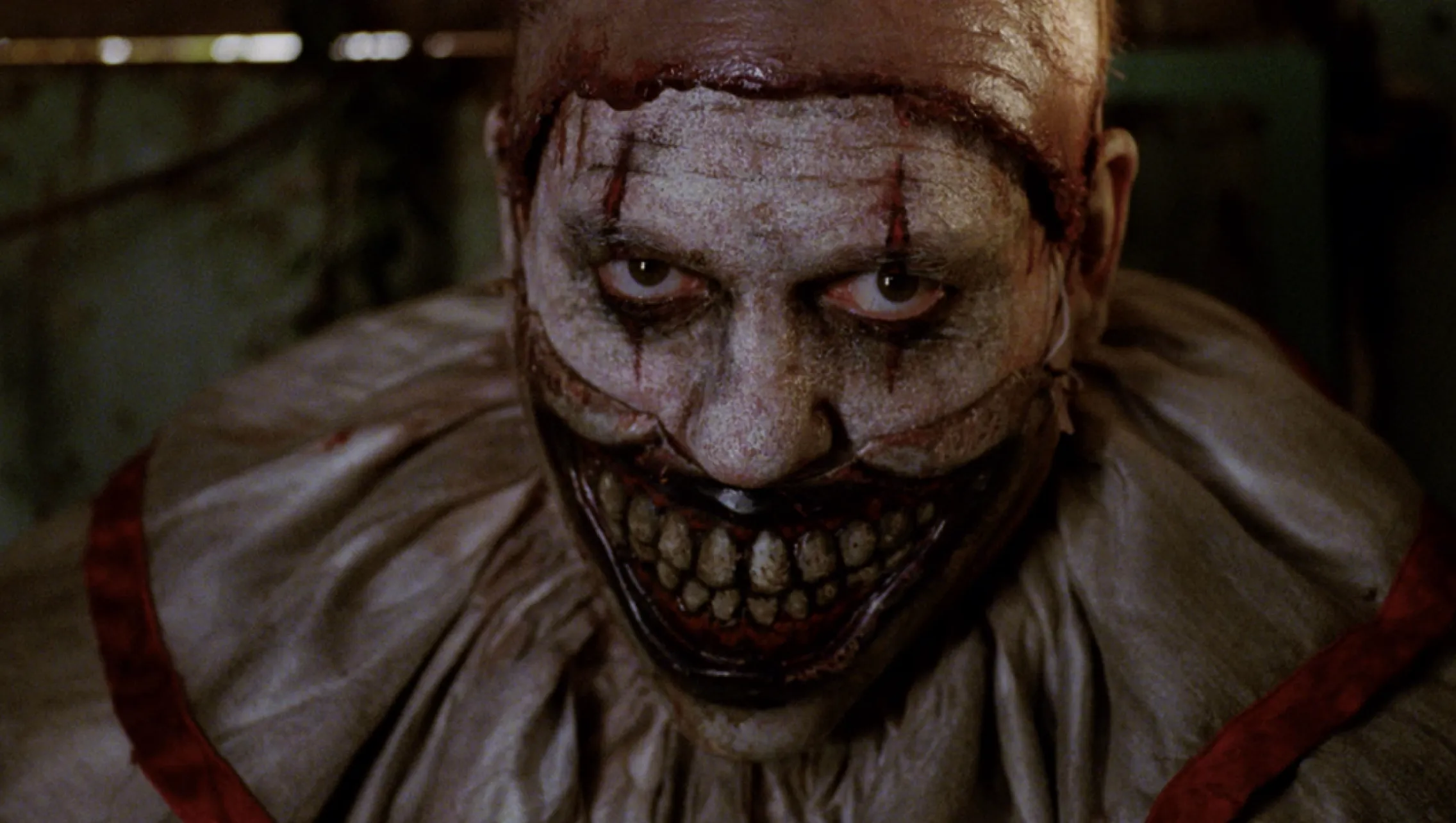 Twisty the Clown, wearing face paint and his grinning mask, stares up at the viewer.
