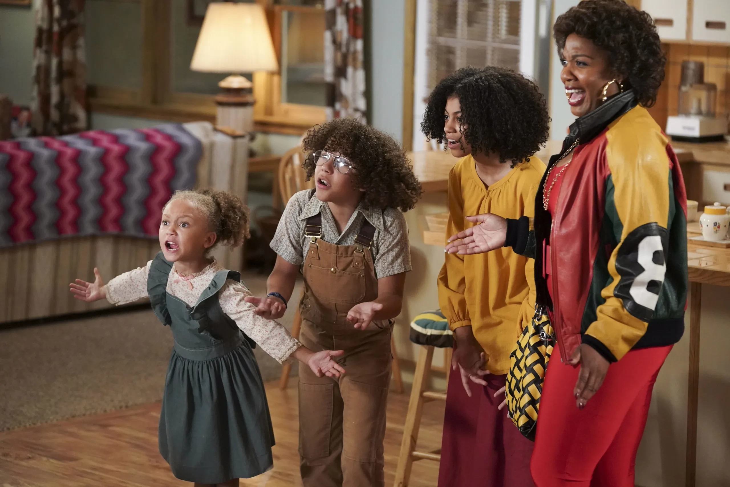 An adult woman and three children reacting to something out of frame. Some with outrage, some with joy