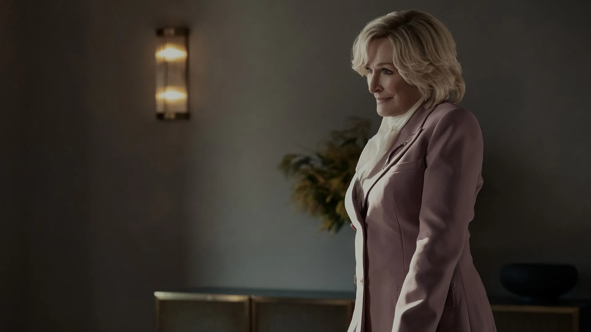  Glenn Close as Dina Standish, wearing a mauve/pink blazer in an office setting