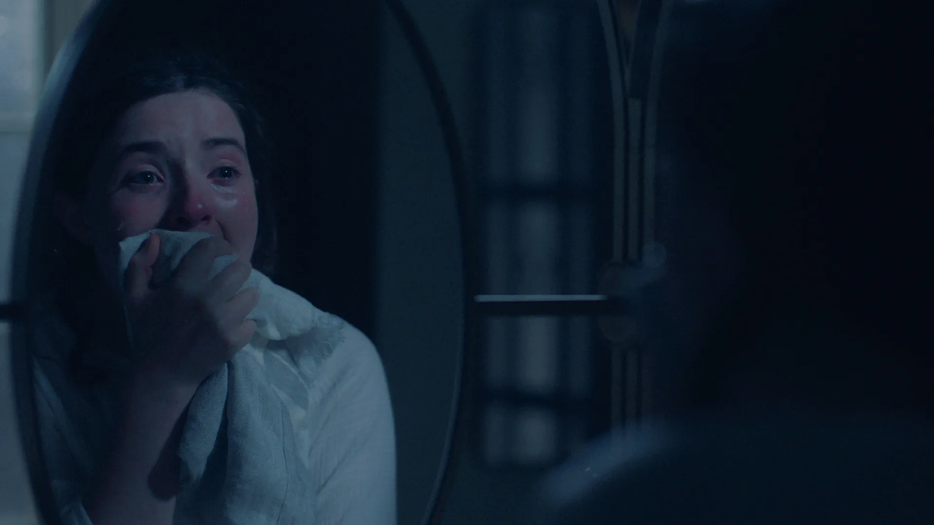 Lucy Halliday as the character Daisy looking shocked in a mirror in The Testaments