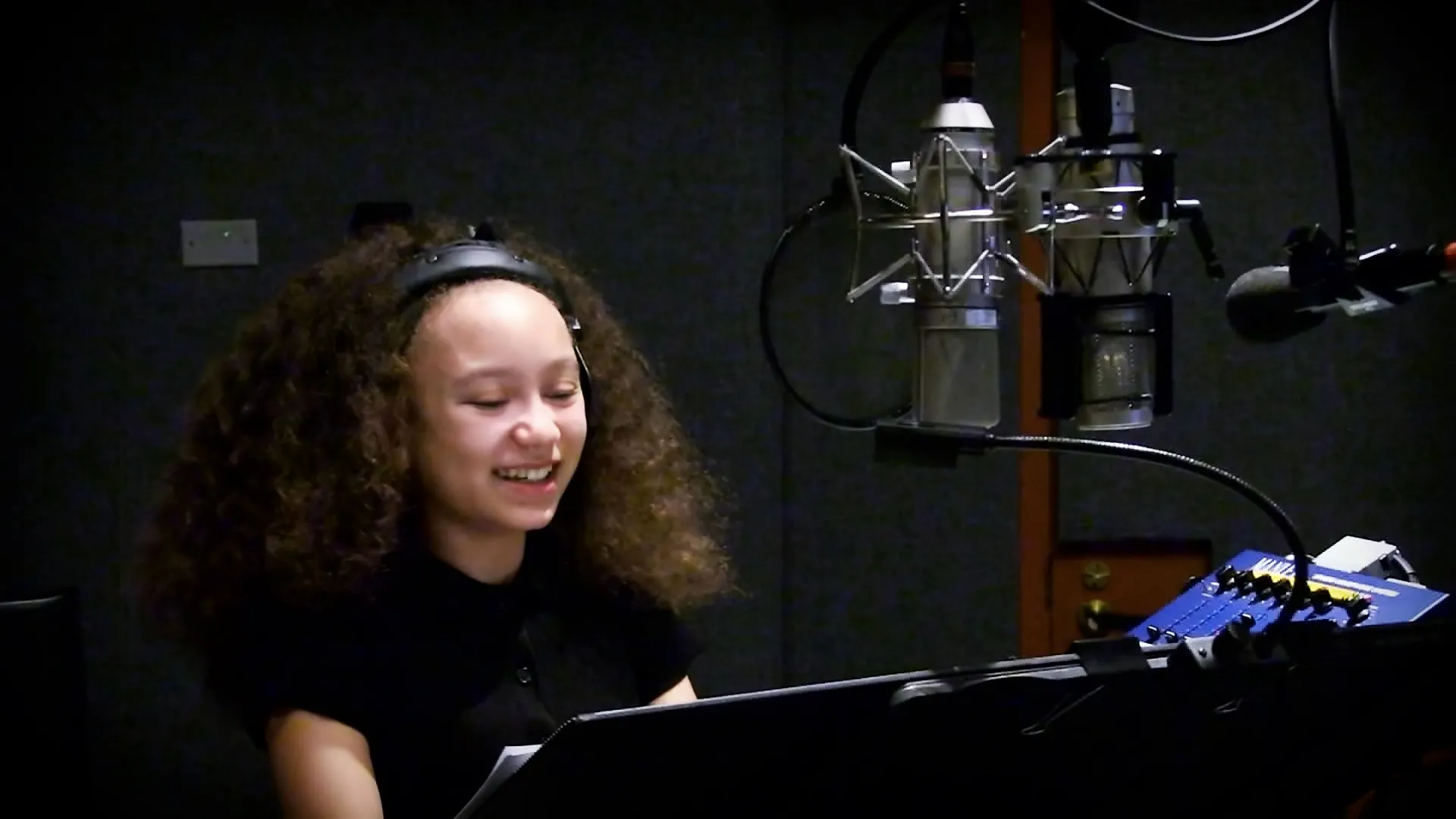 Mykal-Michelle Harris smiles warmly while speaking into a professional studio microphone during a recording session.