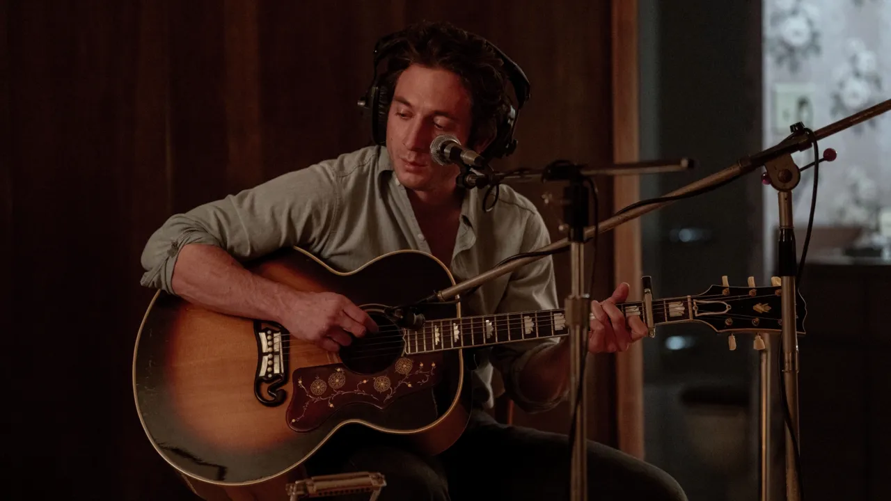 Bruce Springsteen (Jeremy Allen White) plays a guitar in front of a microphone.