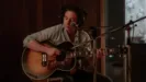 Bruce Springsteen (Jeremy Allen White) plays a guitar in front of a microphone.