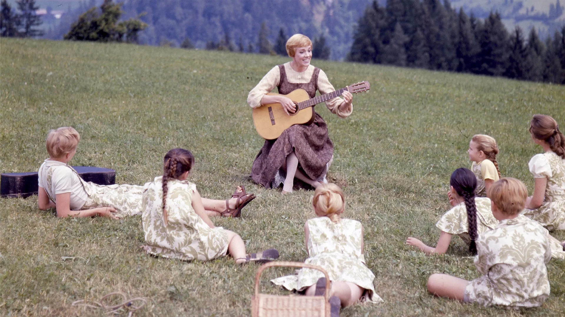 This image captures a iconic moment from the 1965 musical film The Sound of Music, featuring Julie Andrews as Maria von Trapp teaching the von Trapp children the song "Do-Re-Mi" on a hillside in Salzburg, Austria. 