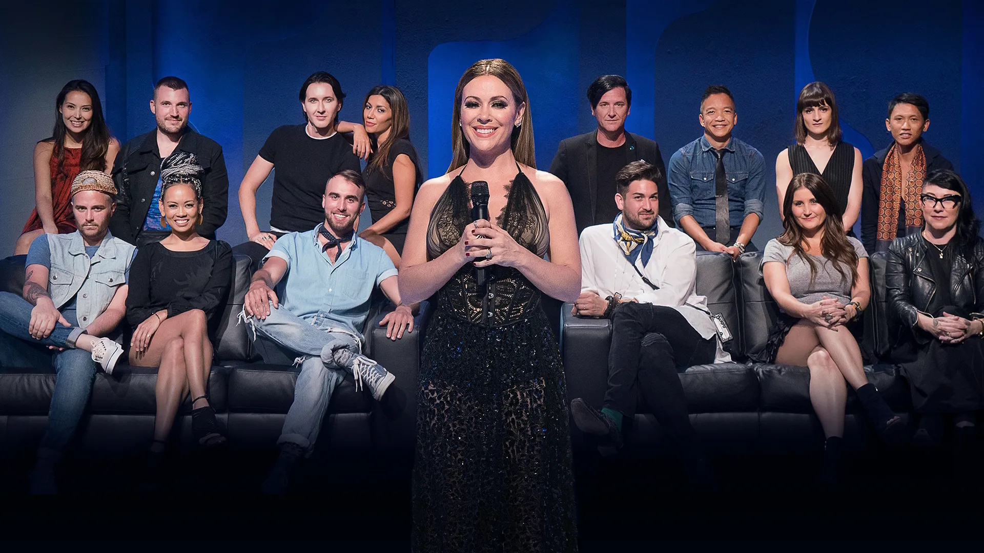 An official promotional cast photo for Project Runway All Stars, featuring host Alyssa Milano standing center holding a microphone, with an ensemble group of contestants seated on leather couches behind her against a blue lit backdrop.