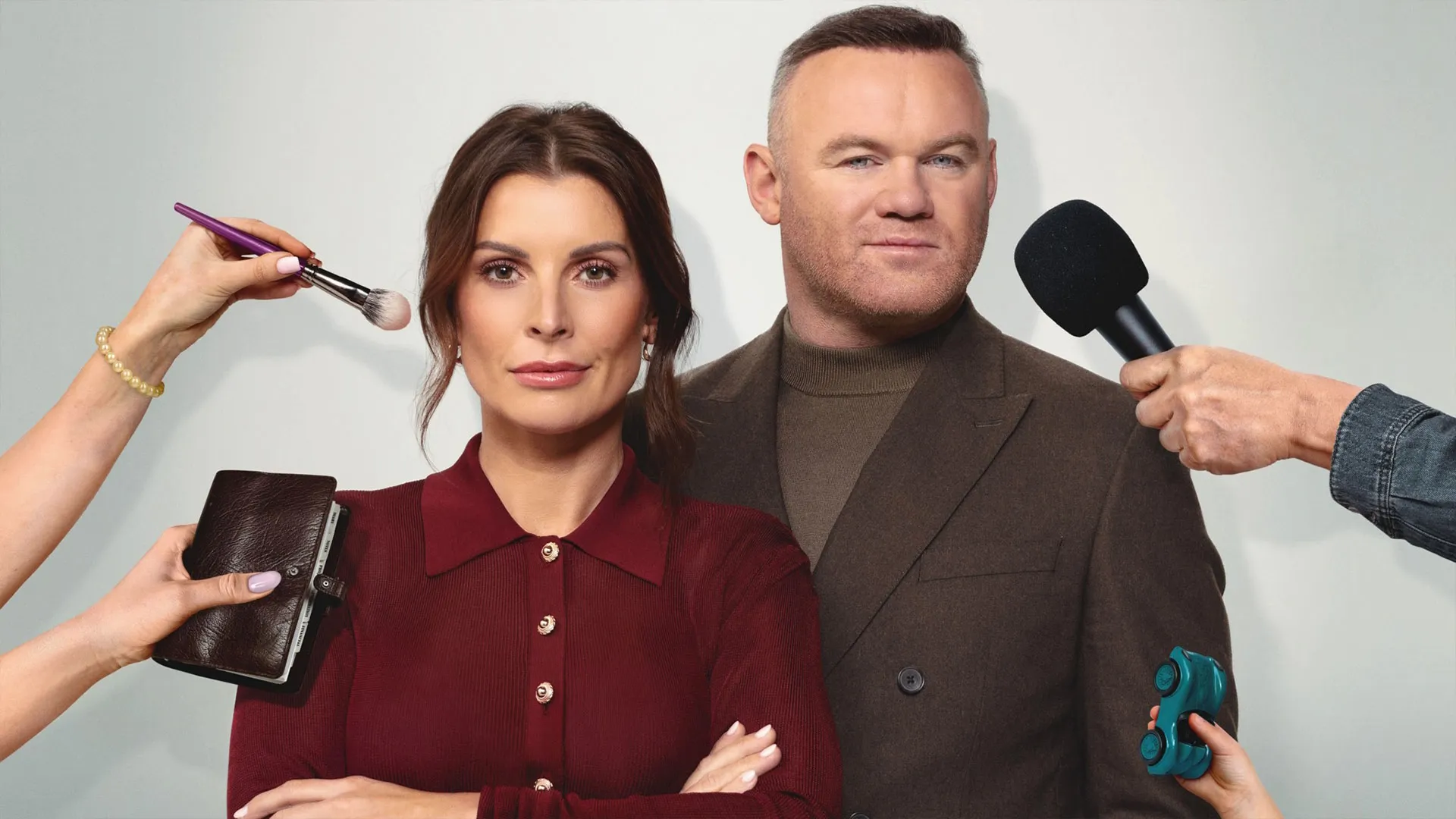Colleen and Wayne Rooney stand side by side while hands from off-camera hold a microphone, makeup brush, wallet and toy car around them.