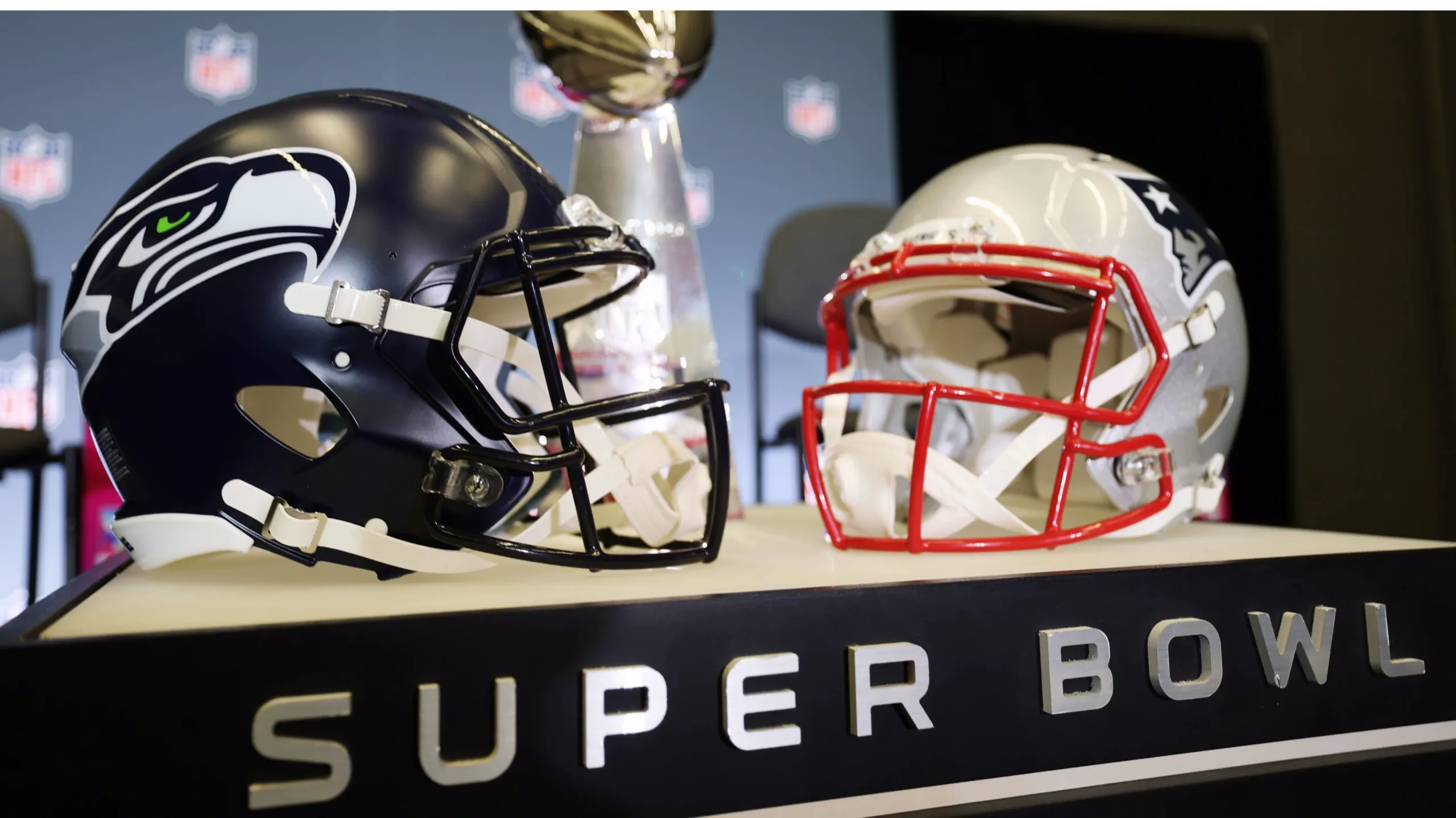 Seattle Seahawks and New England Patriots helmets facing each other with the Lombardi Trophy behind them and ‘Super Bowl’ text in front