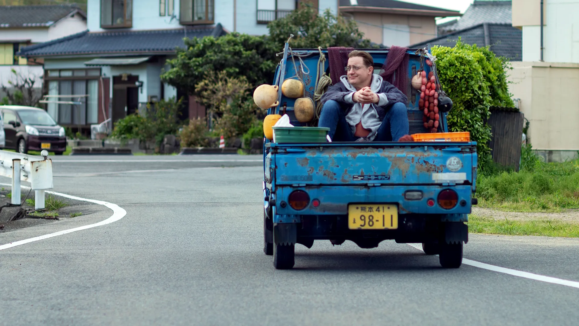 Phillip (Brendan Fraser) is riding in the back of a pickup truck packed with fruits and vegetables