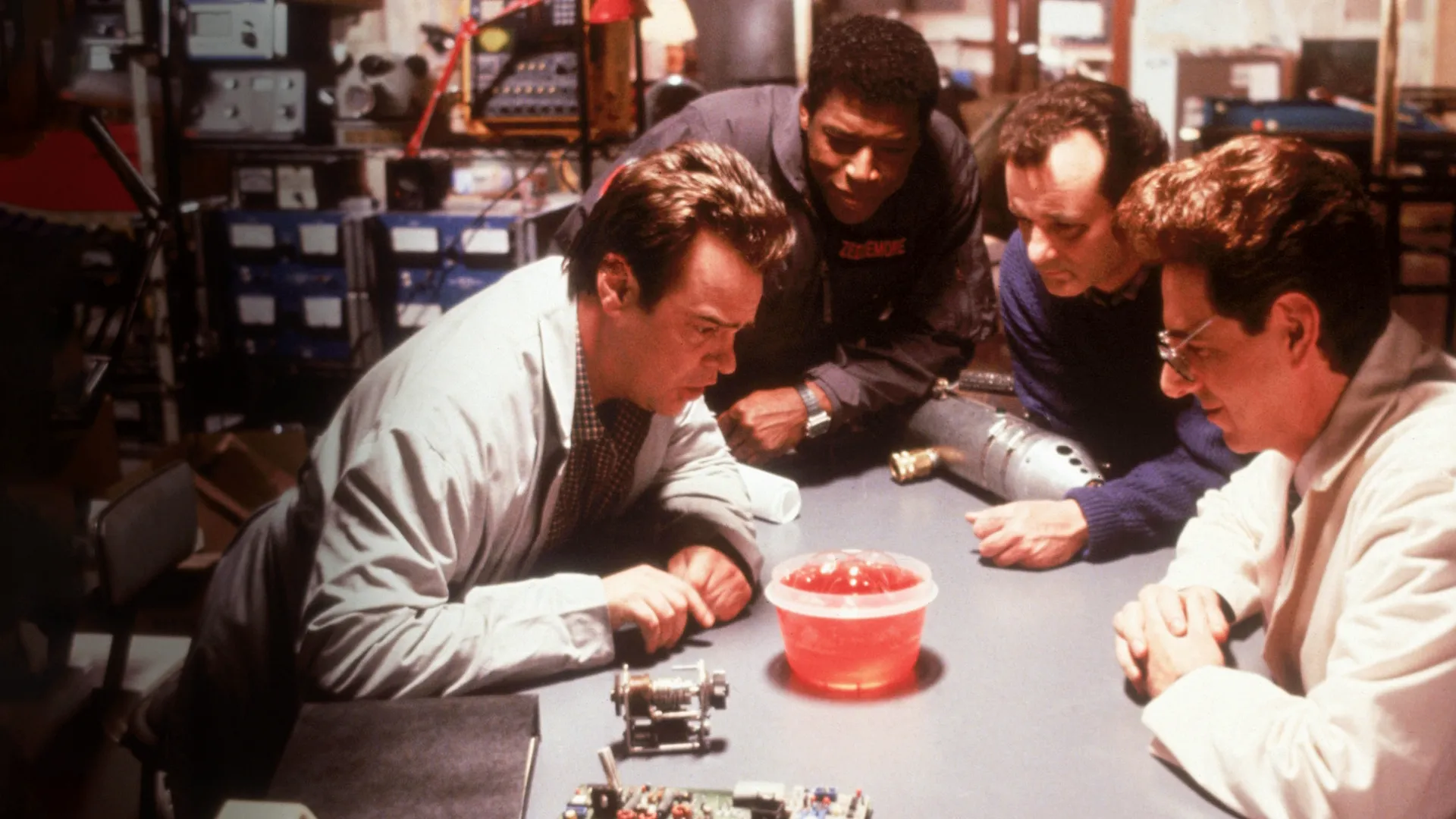 Dan Aykroyd, Ernie Hudson, Bill Murray, and Harold Ramis examining a bowl of glowing pink mood slime in a laboratory scene from Ghostbusters II.
