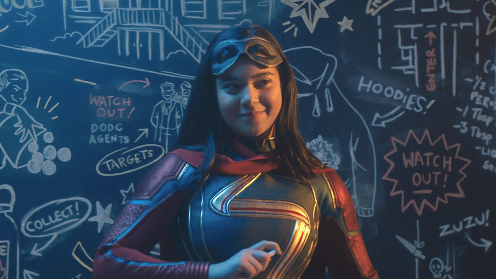 Ms Marvel smiles in front of a doodled blackboard