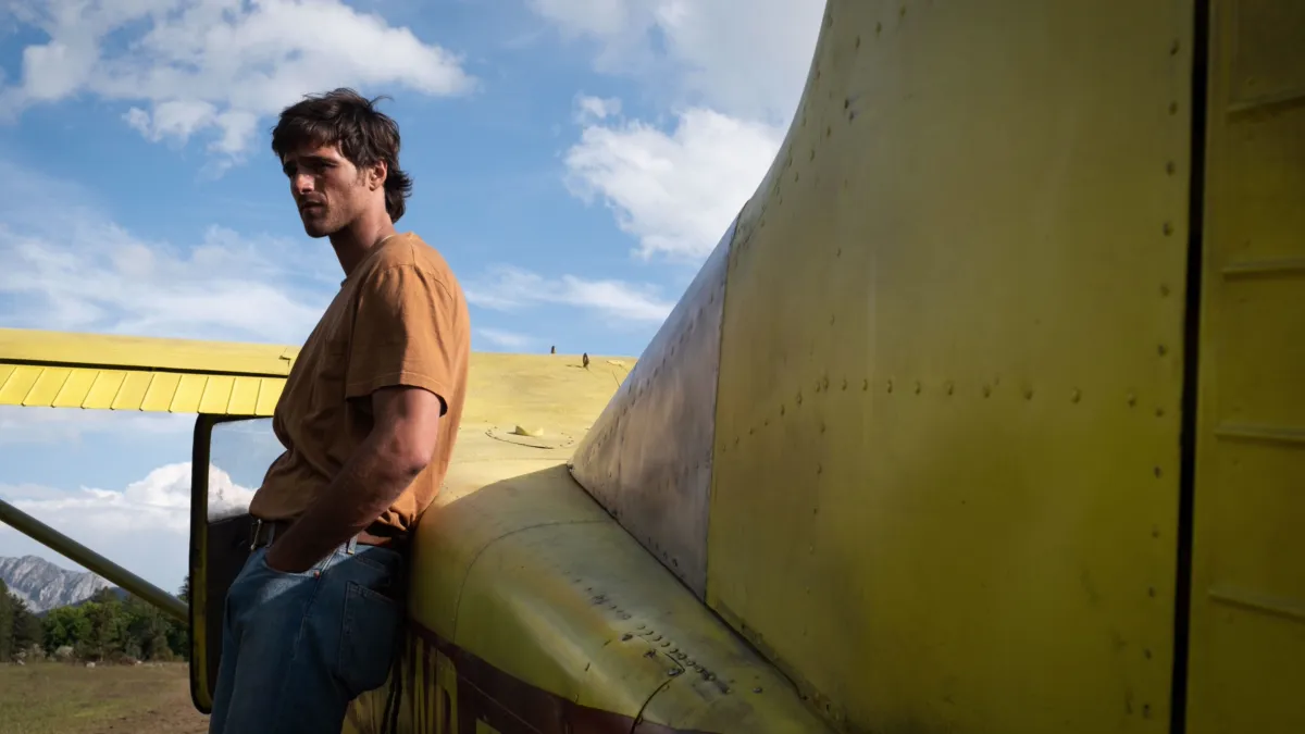 Jacob Elordi leaning against the wing of a small yellow aircraft in a deserted landscape, in The Dog Stars