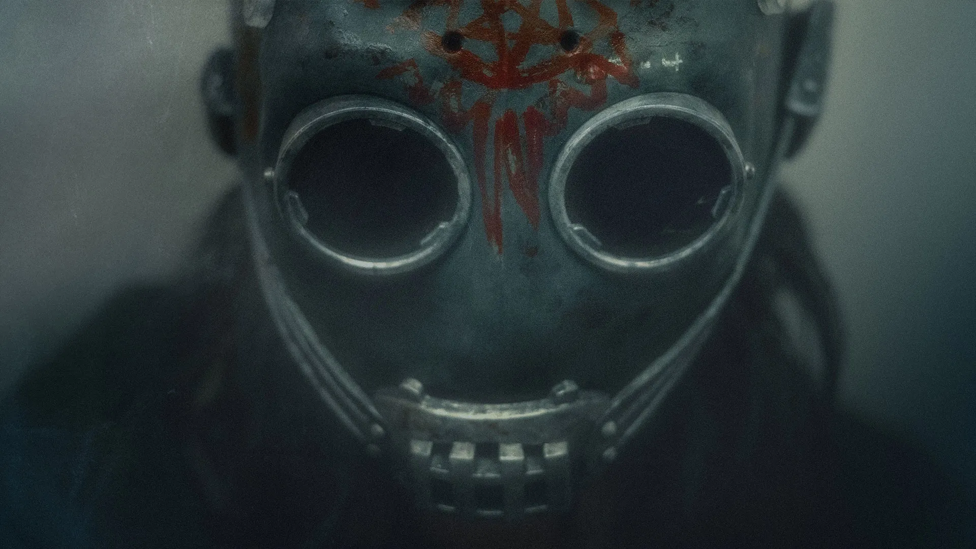 Close-up of a person wearing a weathered metal mask with round eye openings and red painted markings.