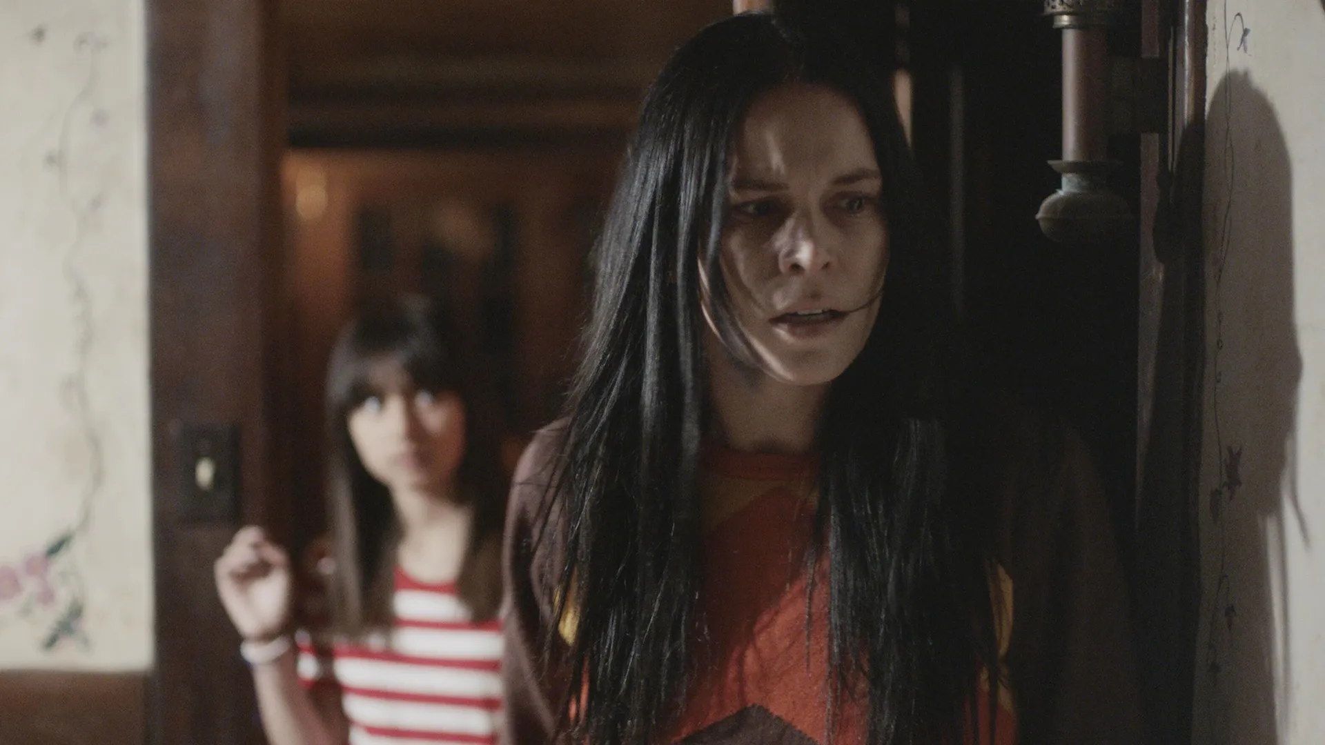 A woman looking flustered, about to look around a corner. Behind her is a 10 year old girl