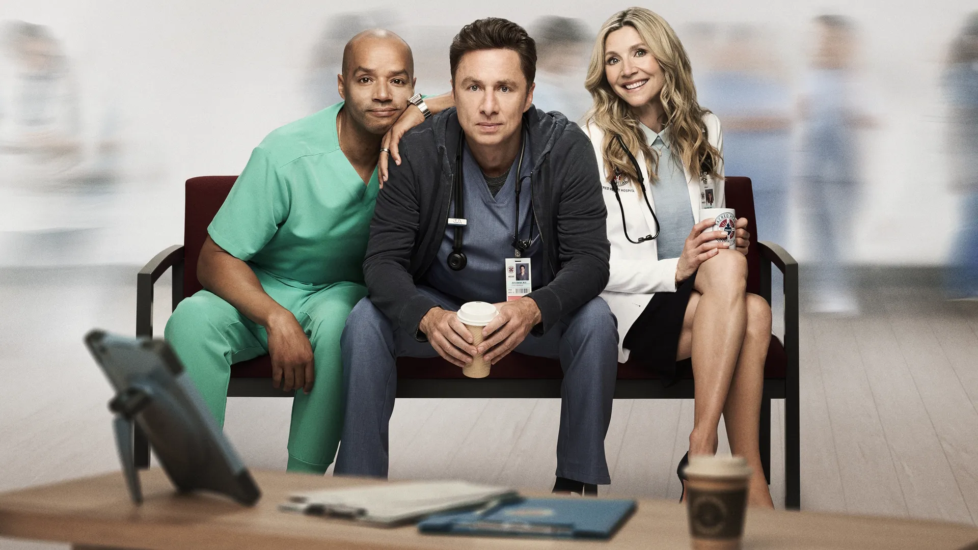 An older J.D., Turk, and Elliot Reid sitting on a waiting room bench in a modern hospital setting from the Scrubs revival.