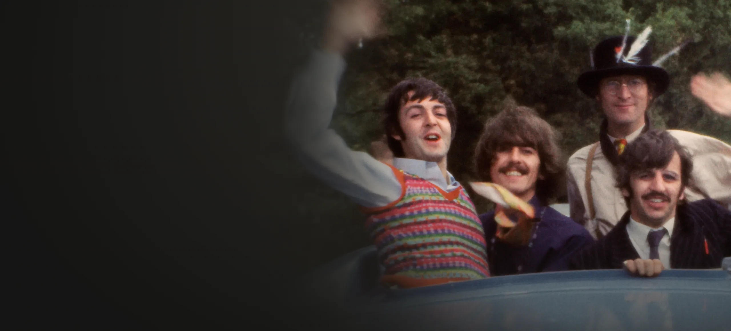 The Beatles leaning out of the sunroof of a car and waving.