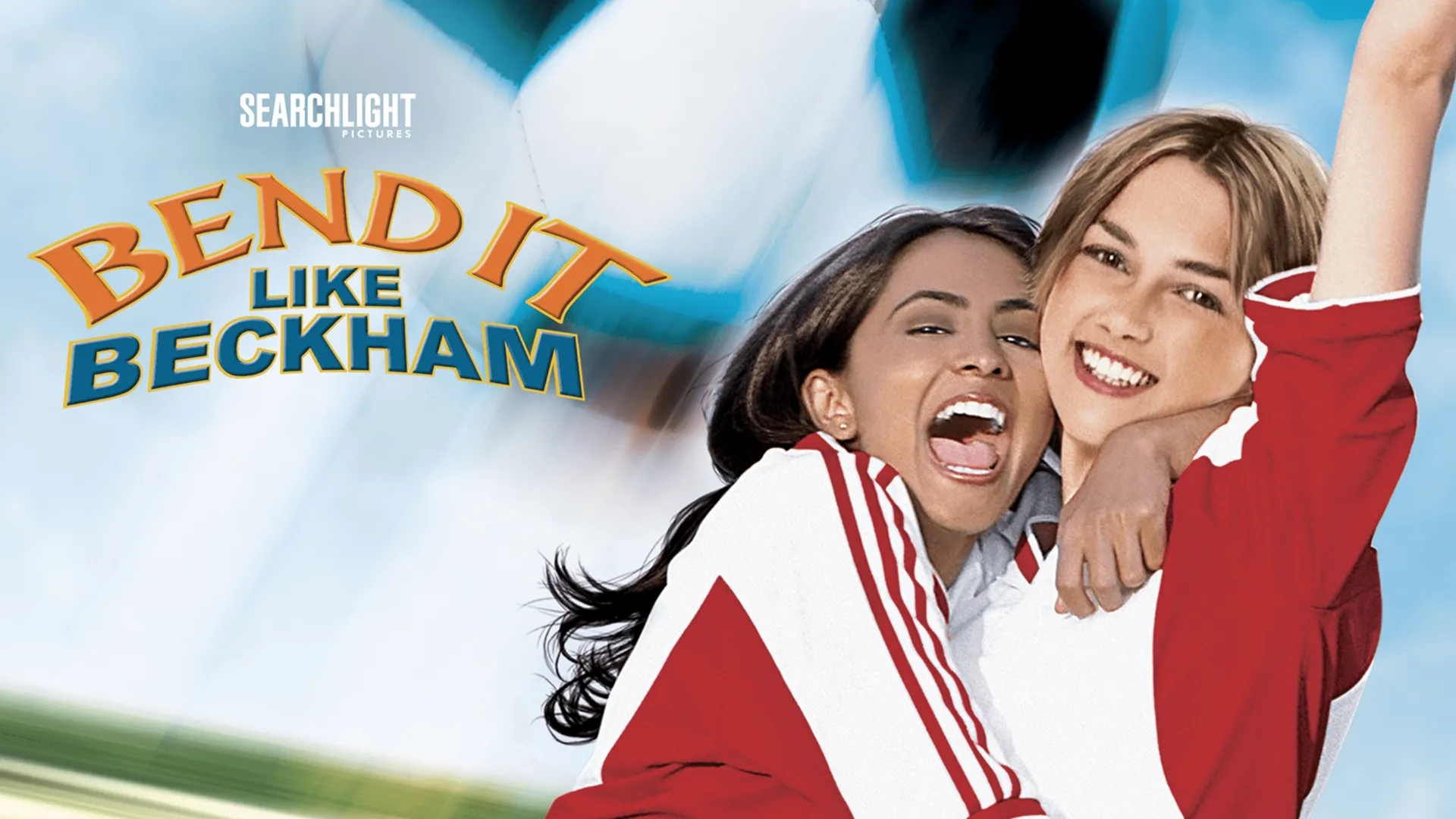 Movie poster for Bend It Like Beckham showing Jess Bhamra (Parminder Nagra) and Jules Paxton (Keira Knightley) in red and white jerseys hugging and smiling ecstatically against a giant blurred soccer ball background.