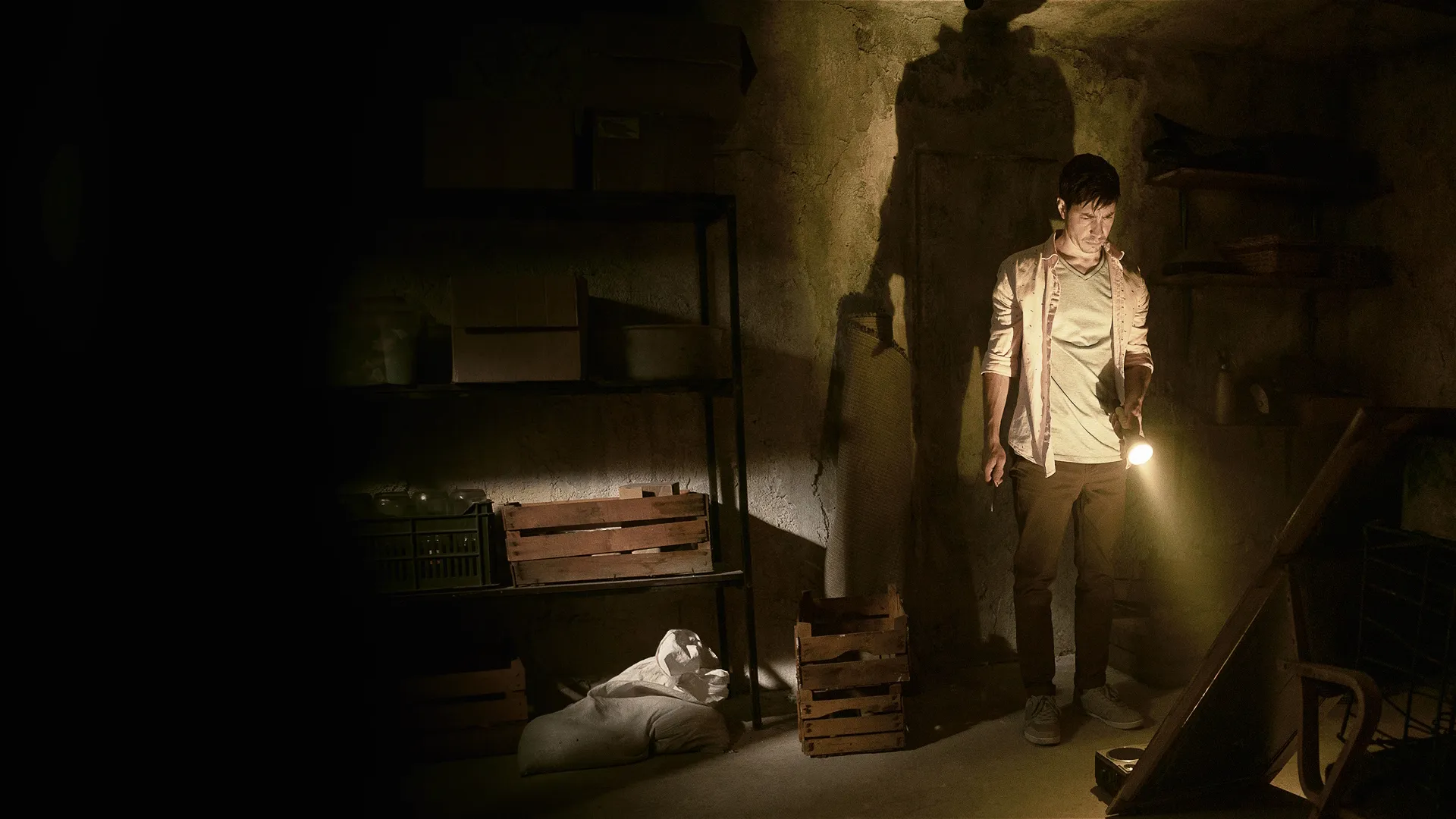 Justin Long exploring a dark, eerie basement with a flashlight in a promotional still from the 2022 horror movie Barbarian.