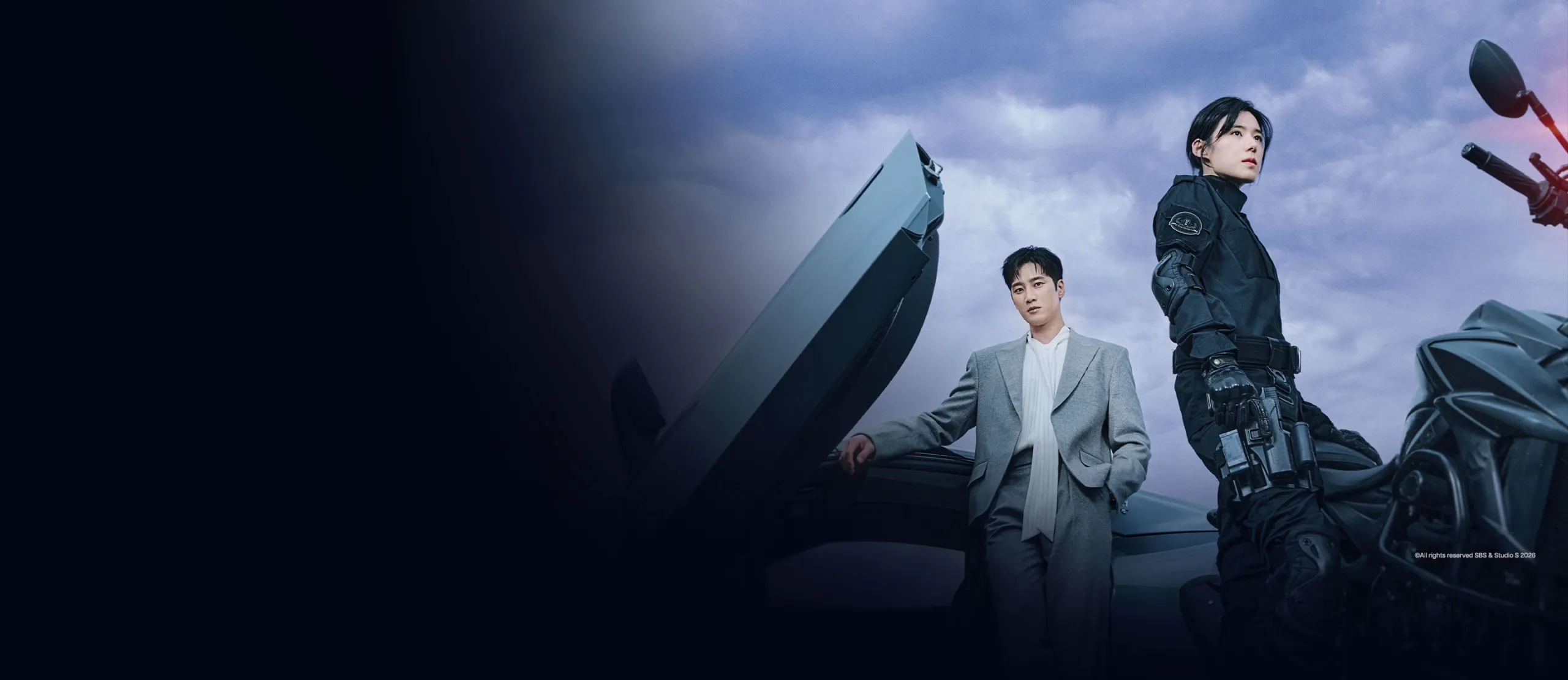 Two people stand beside futuristic vehicles under a cloudy sky, with one wearing tactical gear and the other in a light-colored suit.