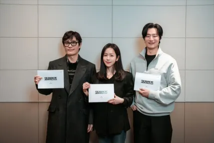 『ザ・コリアンズ（原題）』のプロモーション用キャスト写真。3人のキャストが台本を手に並んで立ち、カメラに向かっている。1990年代初頭の韓国を舞台に、平凡な中流家庭の夫婦を装いながら国家を揺るがす極秘任務を遂行するスパイ夫婦の姿を描くスパイサスペンス作品。