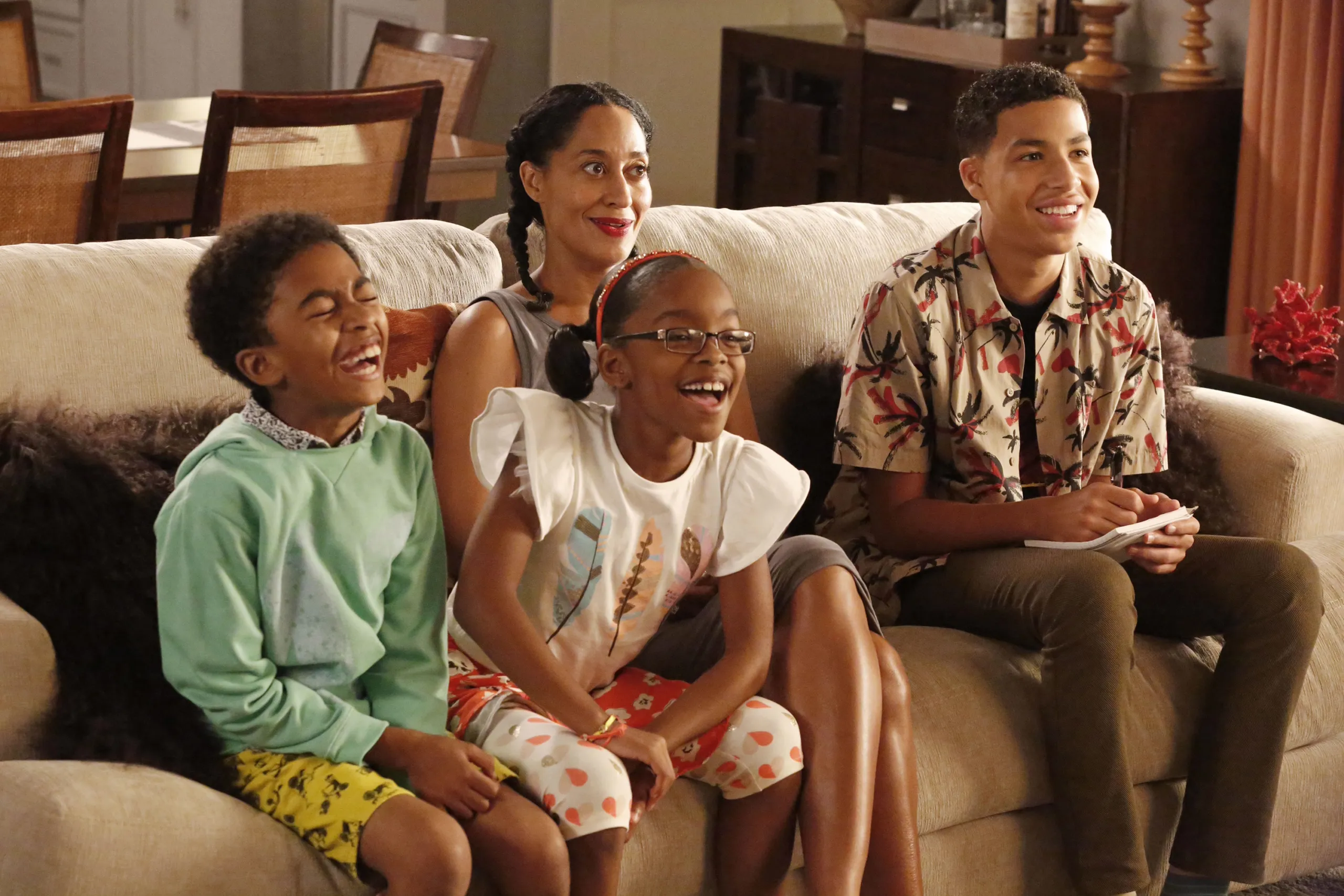 Rainbow Johnson, played by Tracee Ellis Ross sits on a sofa with her three children, laughing and smiling