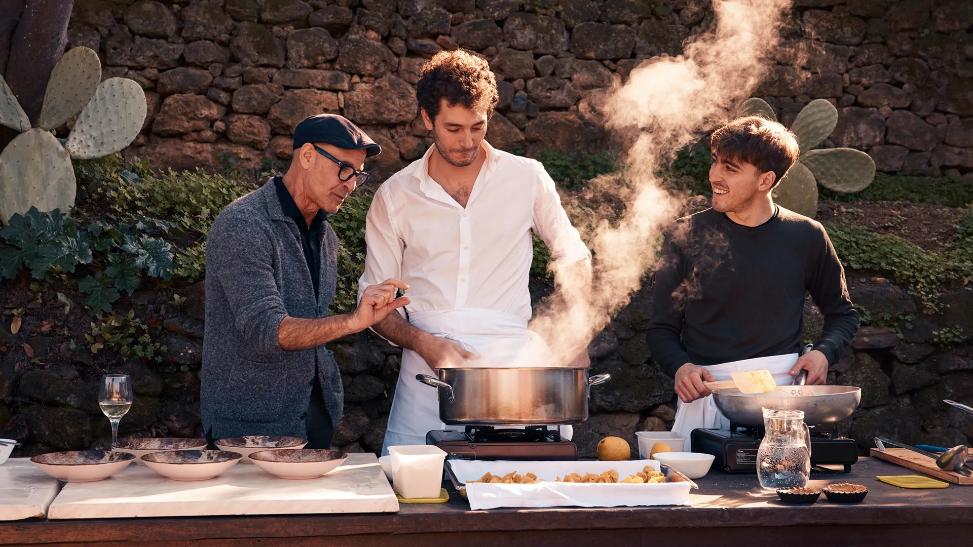 Stanley Tucci and two other men cook in an outdoor kitchen