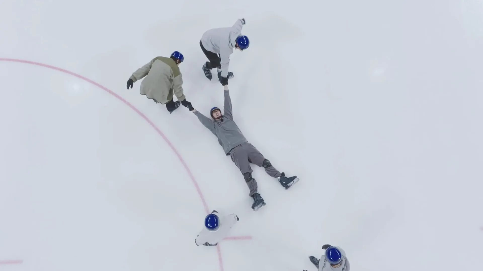 Overhead shot of two people dragging another man across the ice in the middle of an ice hockey rink.
