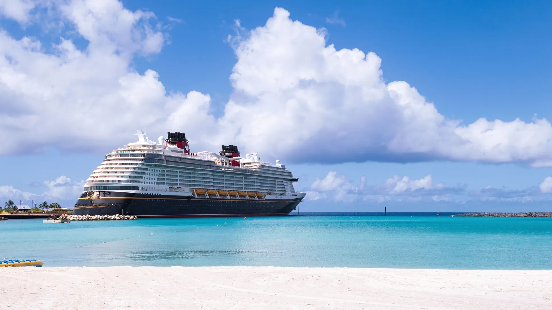A Disney Cruise Line ship off the coast of a white sandy beach