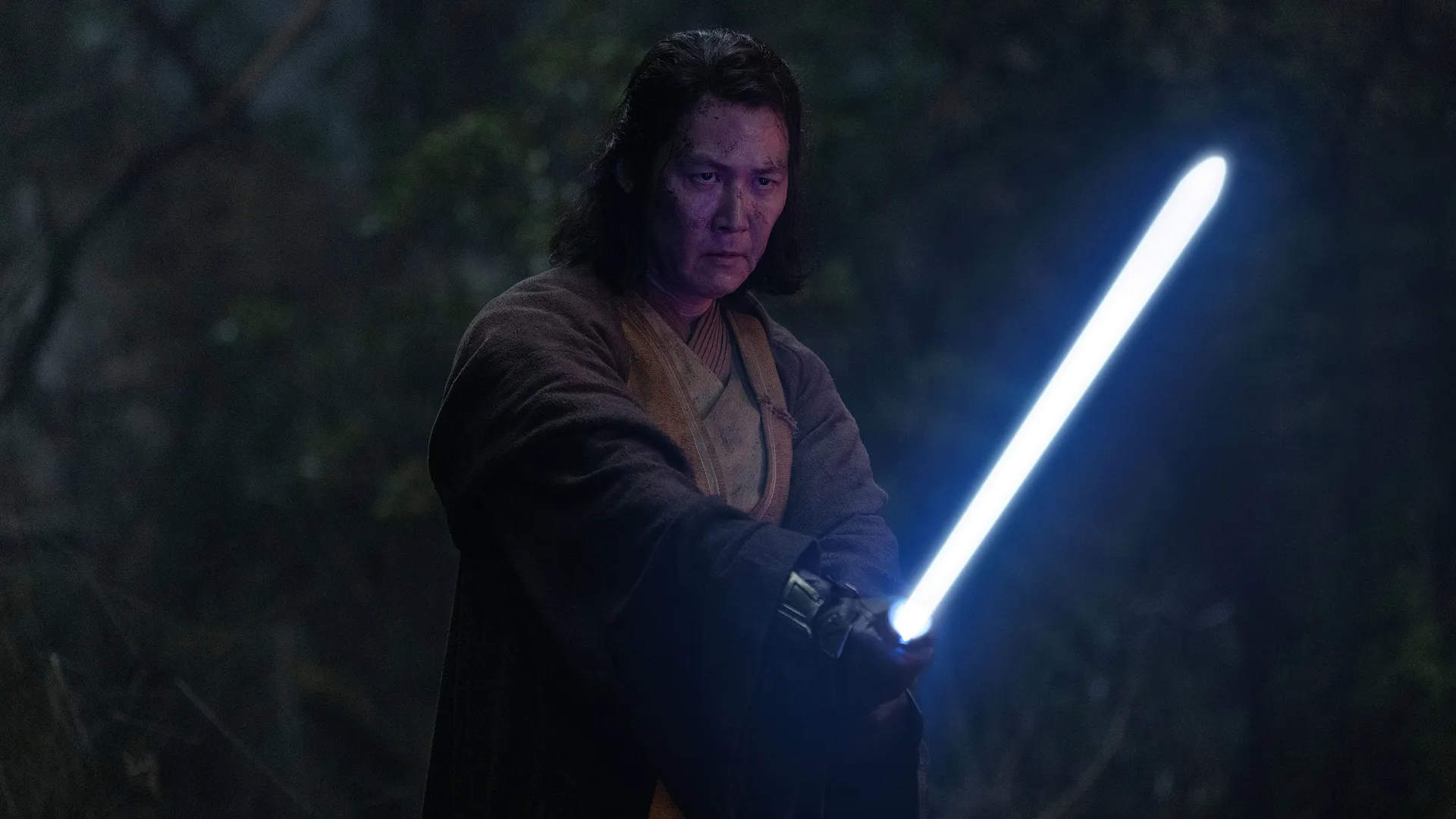 Jedi Master Sol (Lee Jung-jae) wields a blue lightsaber in a dark forest.