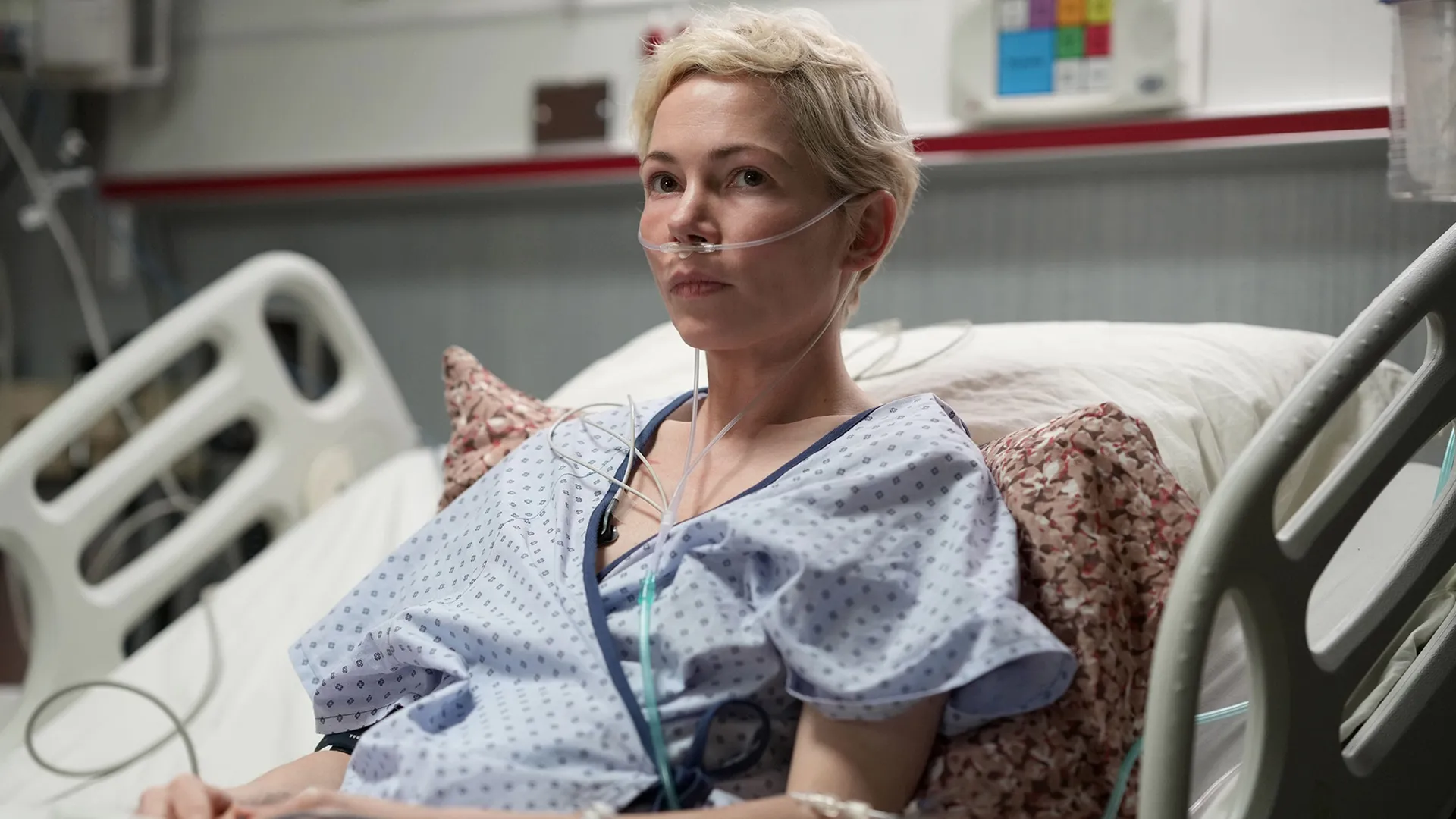 Molly Kochan (Michelle Williams) lies on a hospital bed in a hospital gown, with an oxygen tube attached to her nose