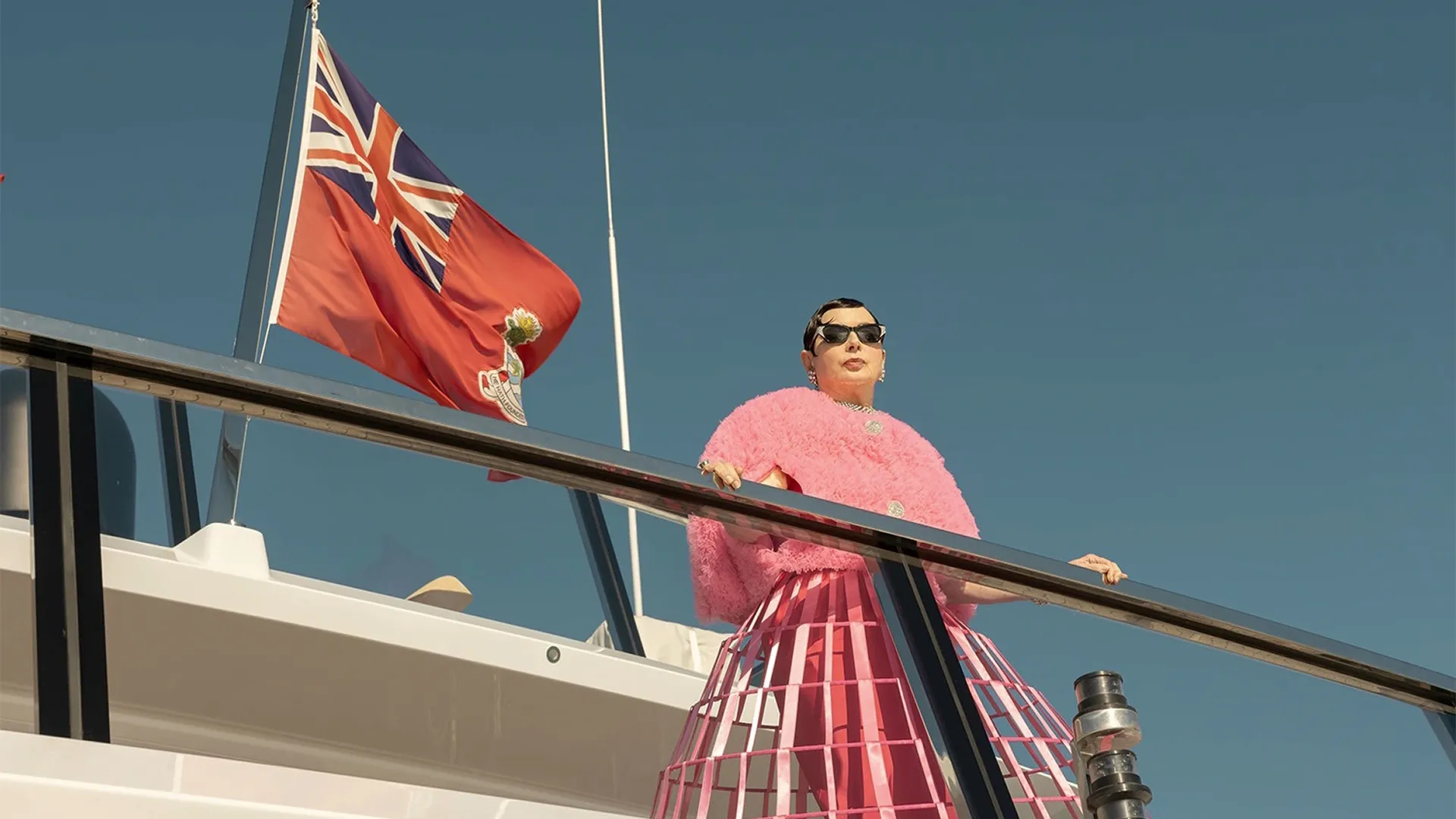 Franny Forst (Isabella Rossellini) stands next to the railing of a yacht flying a British Red Ensign flag.