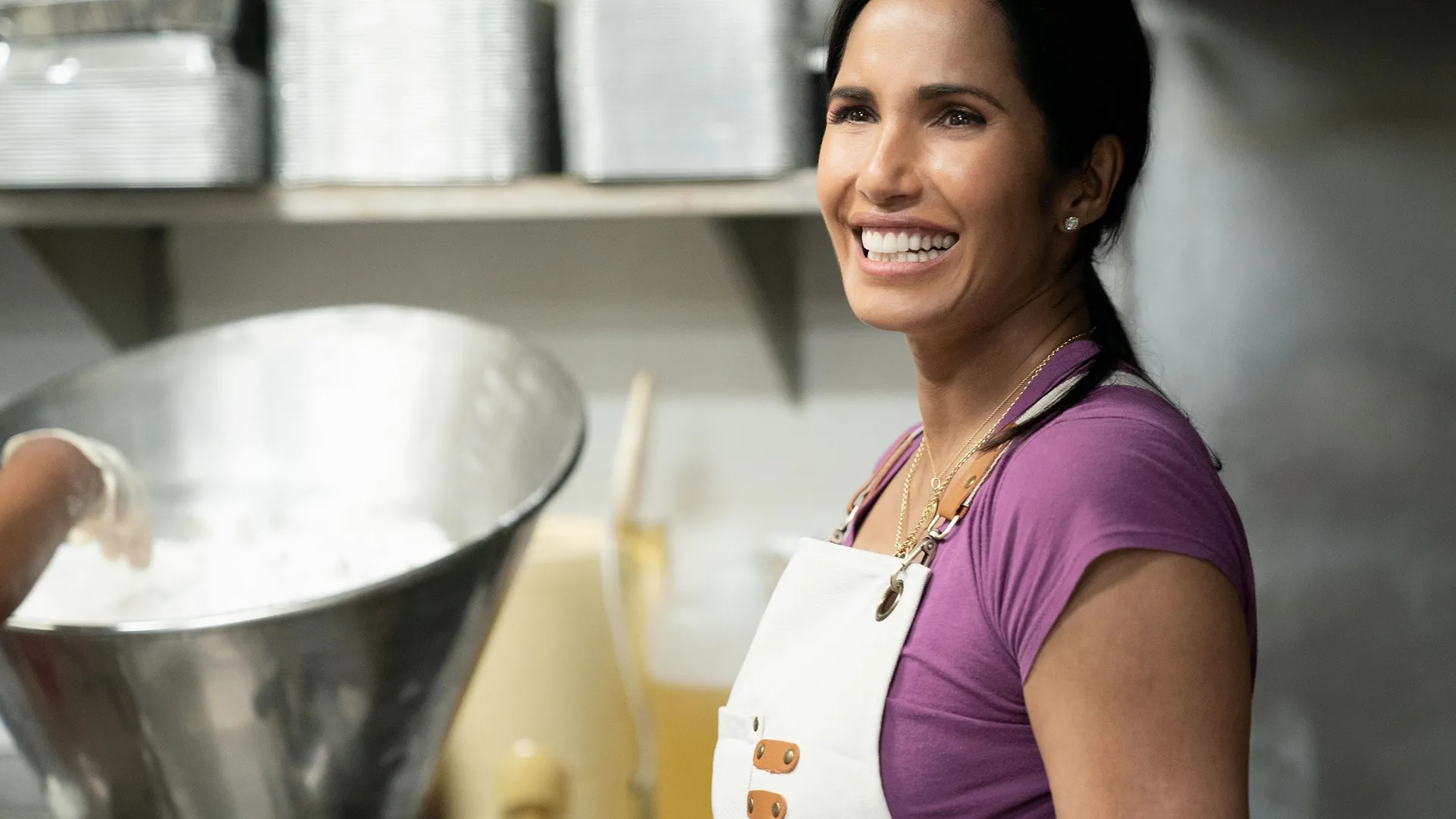 A closeup of Padma Lakshmi smiling inside a kitchen
