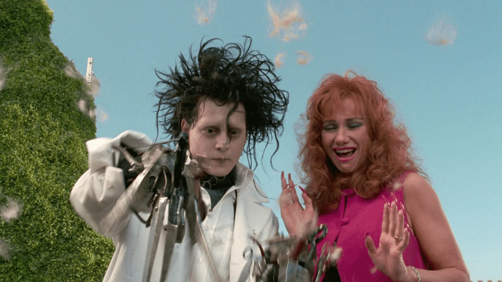 Johnny Depp as Edward Scissorhands using his scissor hands to rapidly trim a hedge while a smiling Kathy Baker as Joyce Monroe stands next to him in a scene from Tim Burton's 1990 movie Edward Scissorhands.