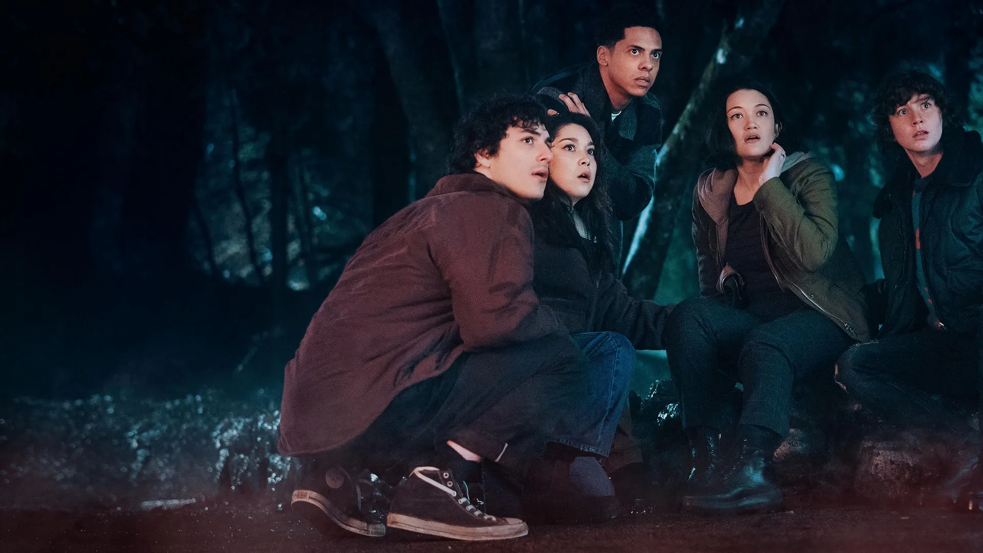 Lucas Parker (Will Price), Margot Stokes (Isa Briones), Isaiah Howard (Zack Morris), Isabella (Ana Yi Puig), and James (Miles McKenna) huddle together in a dark forest at night, staring upward with terrified and wide-eyed expressions.
