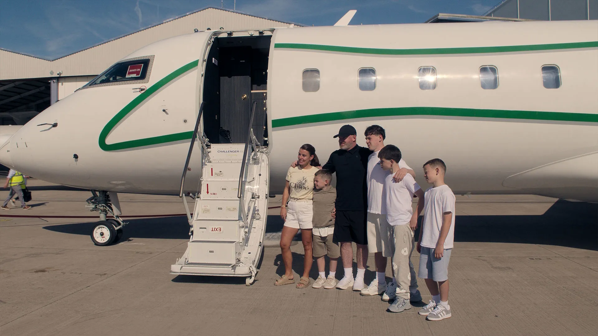Wayne Rooney, Coleen Rooney and their children stand beside a private aircraft in The Real Rooneys.